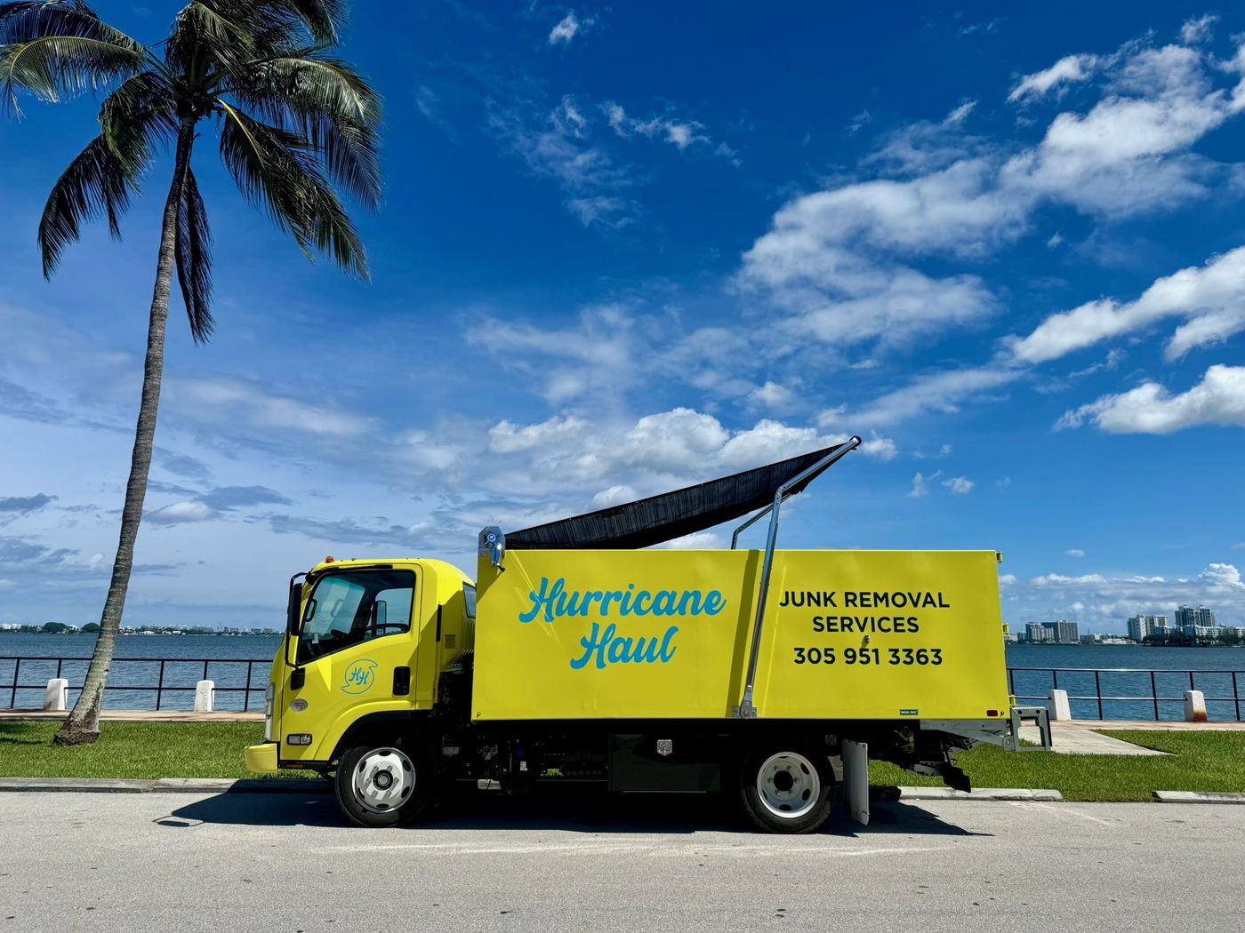 Camión amarillo de Hurricane Haul frente a la bahía de Biscayne, junto a una palma